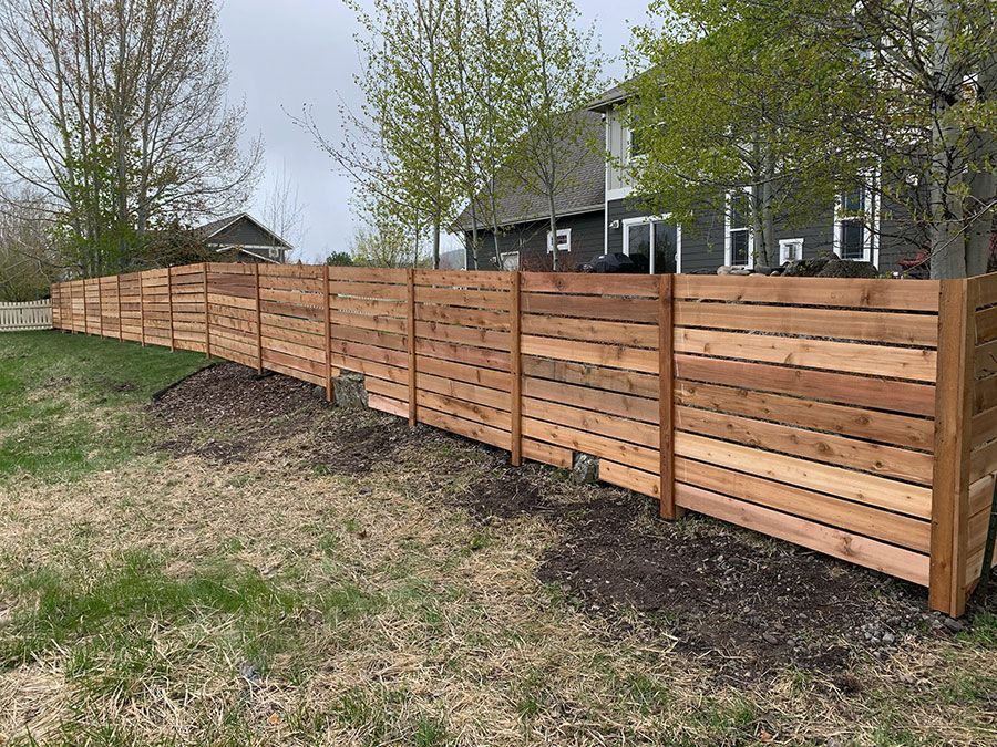 A wooden fence is sitting in the middle of a grassy field in front of a house.