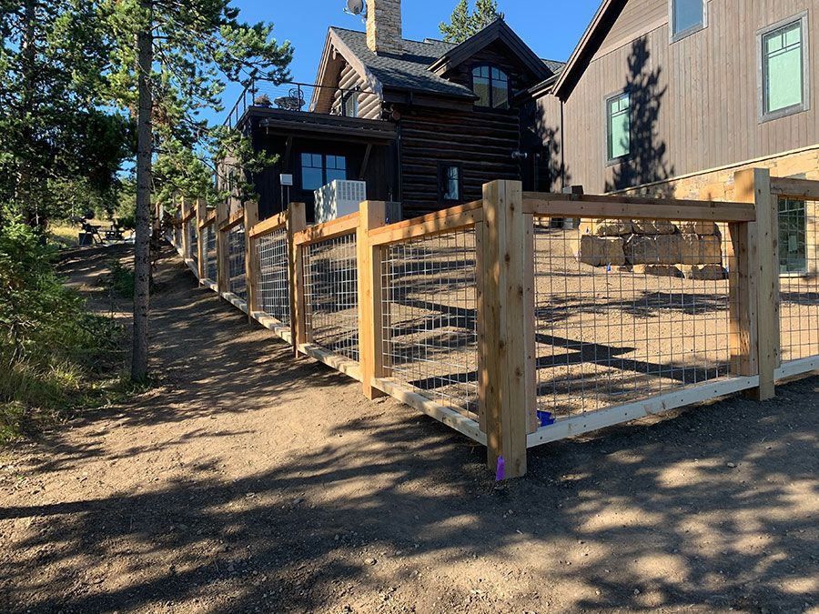A wooden fence surrounds a dirt road in front of a house.