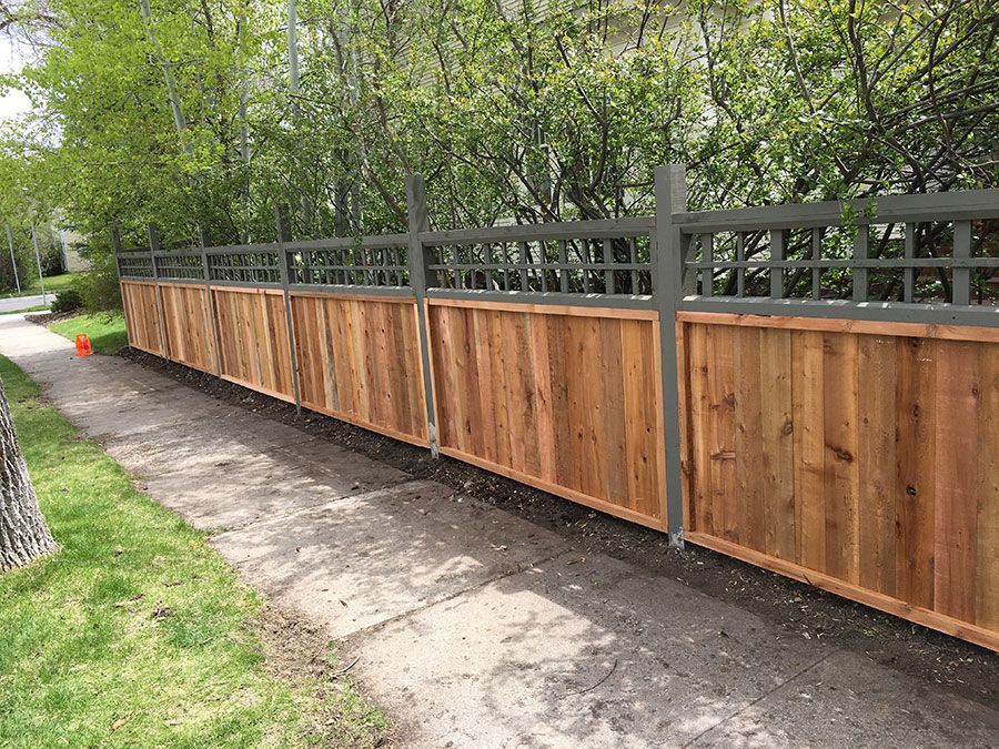 A wooden fence along a sidewalk with trees in the background.