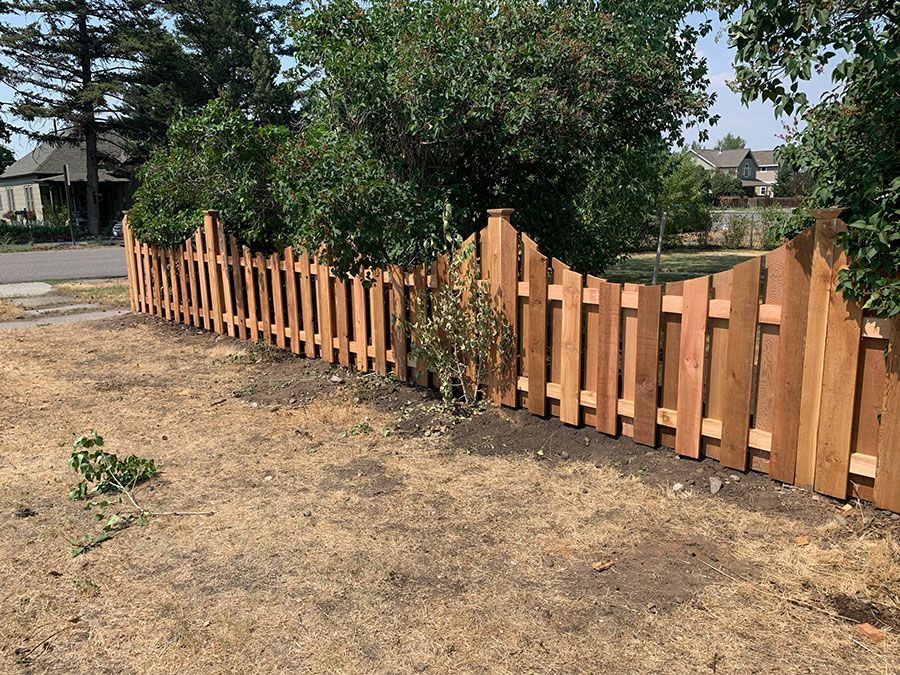 A wooden picket fence is surrounded by trees in a yard.