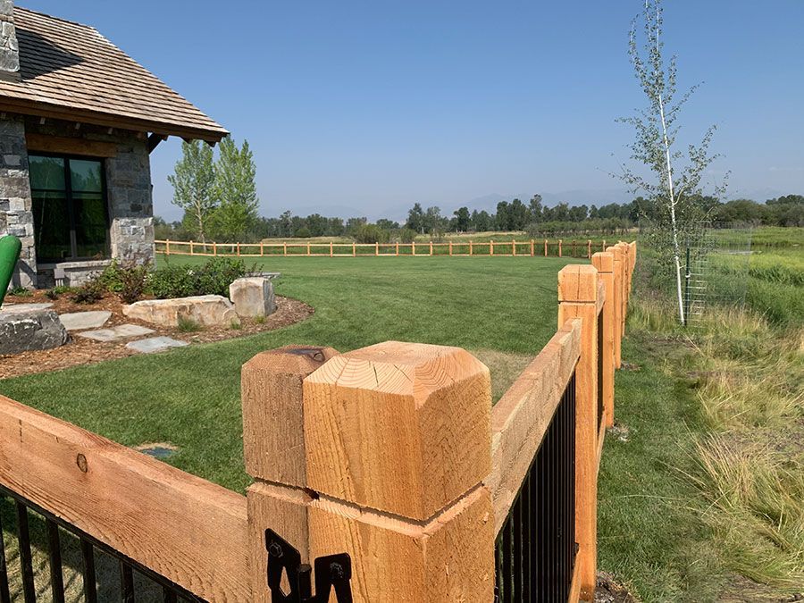 A wooden fence surrounds a lush green field in front of a house.