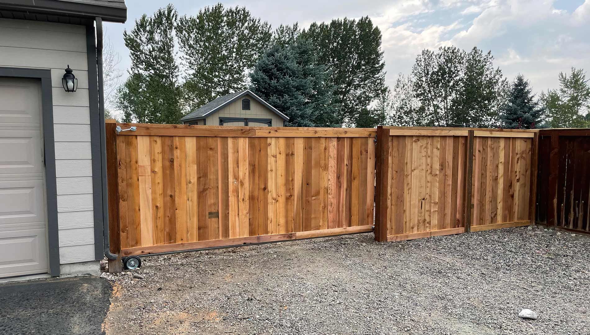 A wooden fence is sitting in front of a garage next to a house.