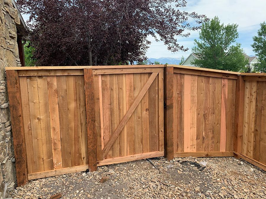 A wooden fence with a gate is sitting on top of a gravel lot.