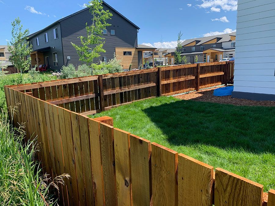 A wooden fence surrounds a lush green yard in front of a house.