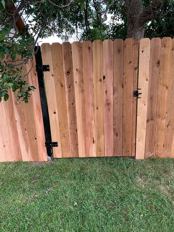 A wooden fence with a black gate is sitting on top of a lush green lawn.