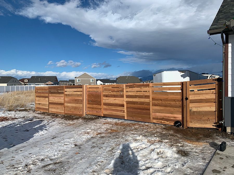 A wooden fence is sitting in the snow next to a house.
