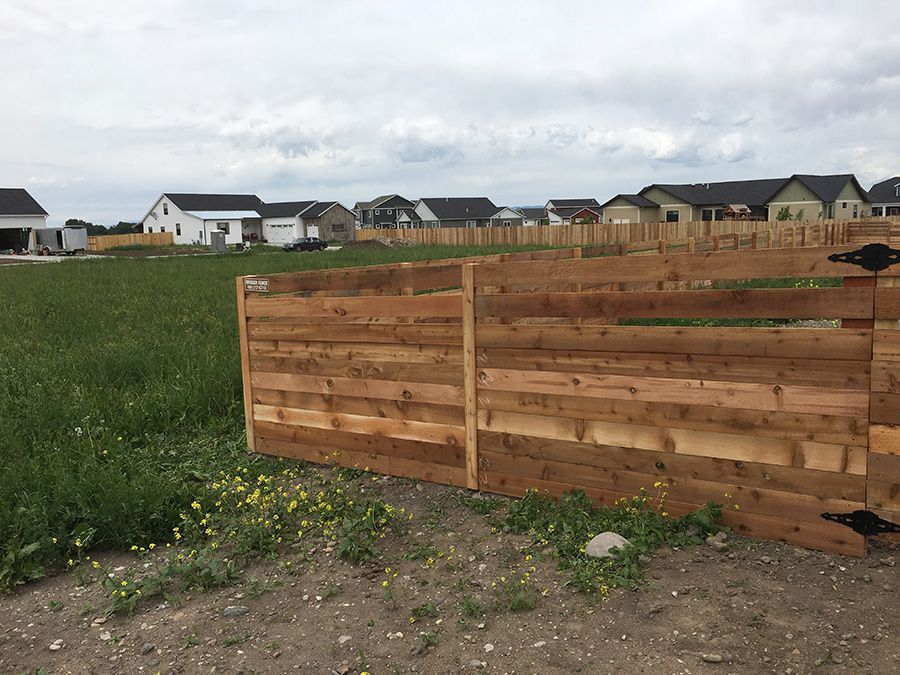 A wooden fence surrounds a field with houses in the background.