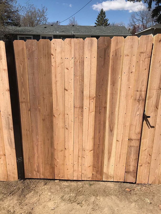 A wooden fence is sitting in the dirt in front of a house.