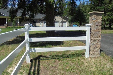 A white fence with a brick post in front of a house.