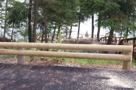 A wooden fence surrounds a dirt road with trees in the background