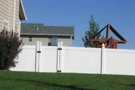 A white fence surrounds a lush green yard in front of a house.