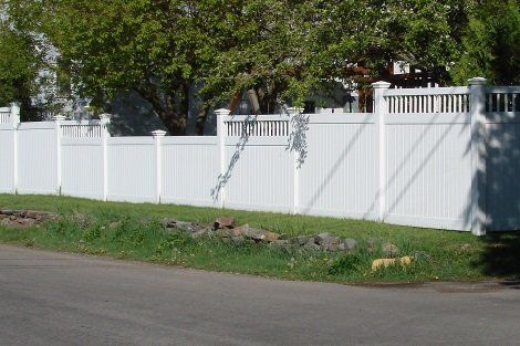 A white fence surrounds a grassy area next to a road.