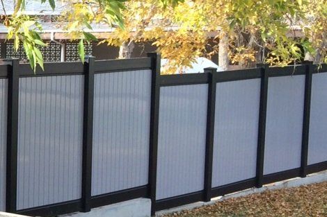A gray and black fence with a tree in the background.