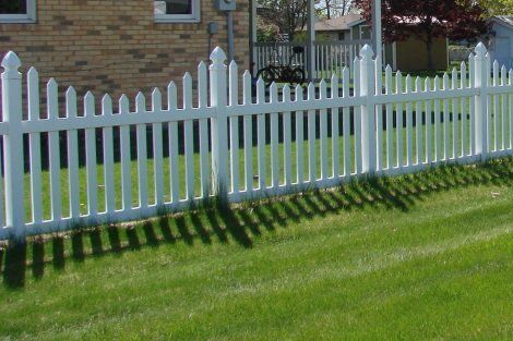 A white picket fence surrounds a lush green lawn in front of a brick house.