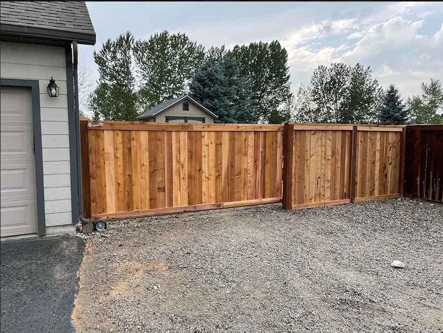 A wooden fence is surrounding a gravel driveway in front of a house.