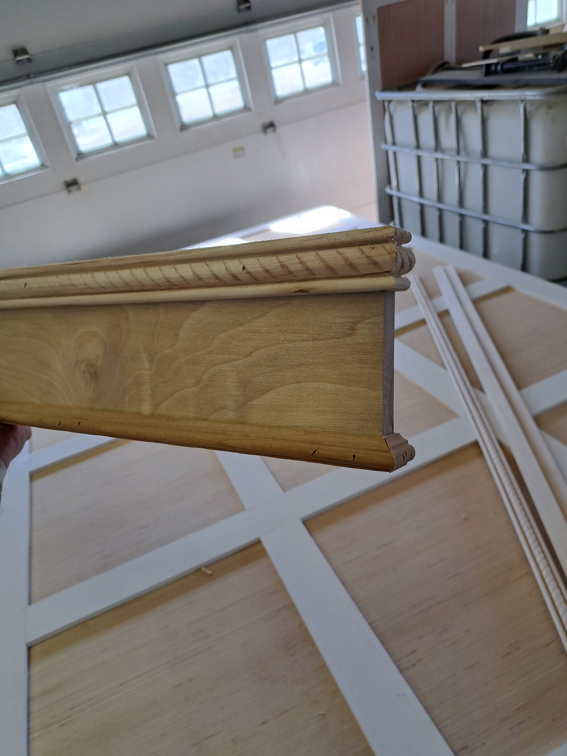 Close-up of a yellow decorative molding board in a bright workshop with windows and lumber stacks