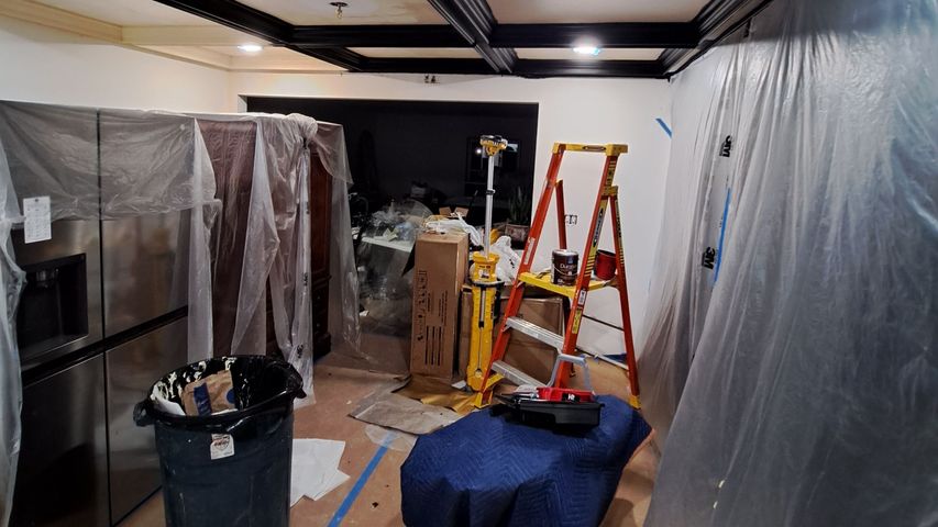 Renovation area with plastic-covered walls, ladder, tools, and boxes in a dim hallway