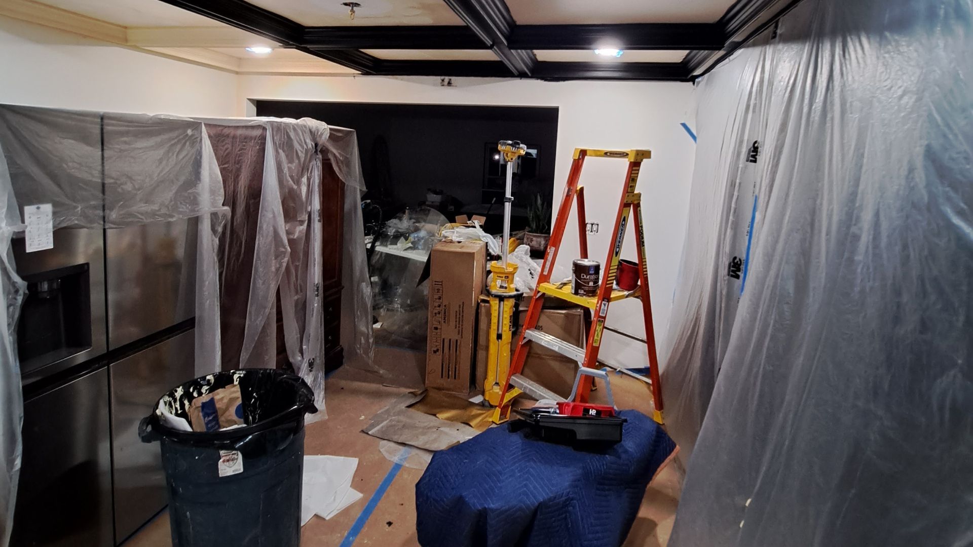 Renovation room with plastic-covered walls, ladder, boxes, and a trash bin on the floor
