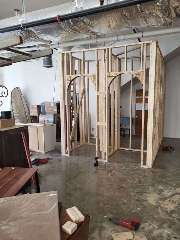 Framed drywall in a basement under construction with exposed beams, tools, and debris on the floor