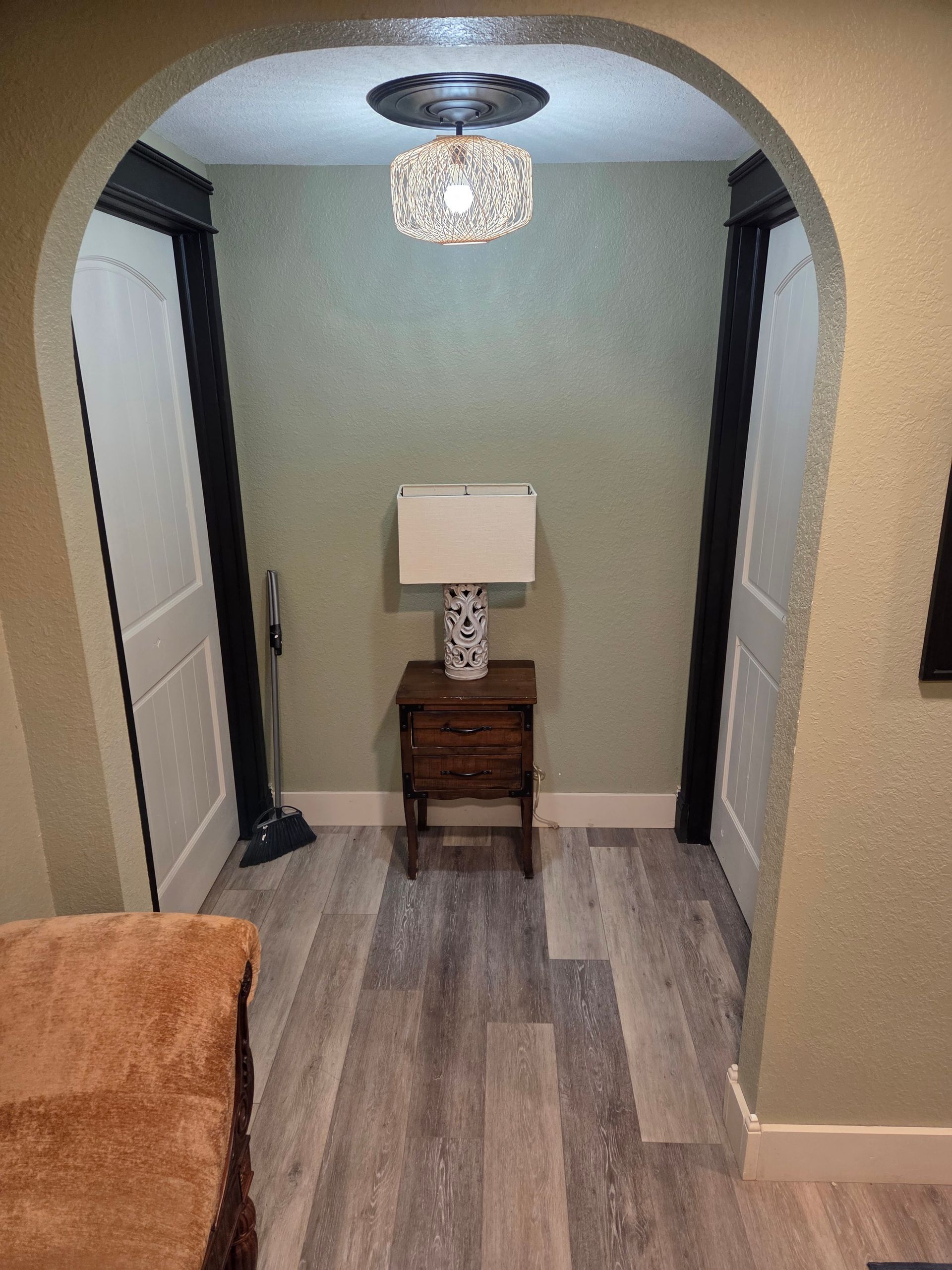 Narrow hallway alcove with a small wooden table, lamp, and crystal ceiling light, framed by arched walls.