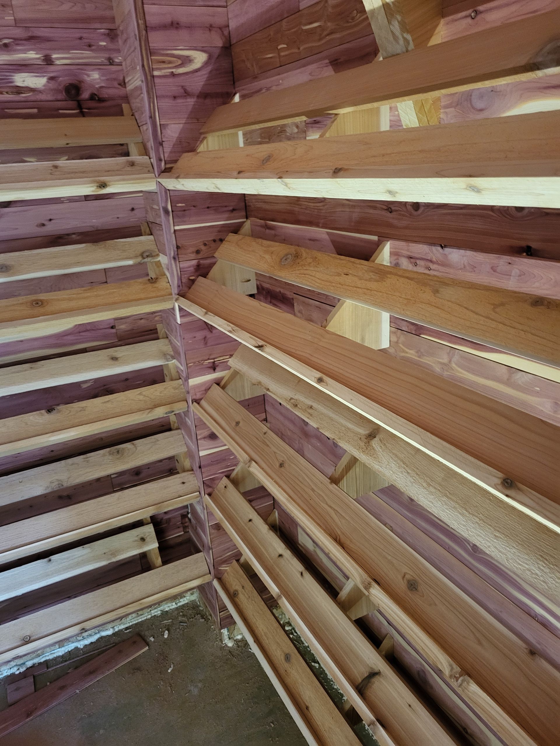 Interior corner of a wooden structure with horizontal slats and exposed beams in pink and natural wood tones