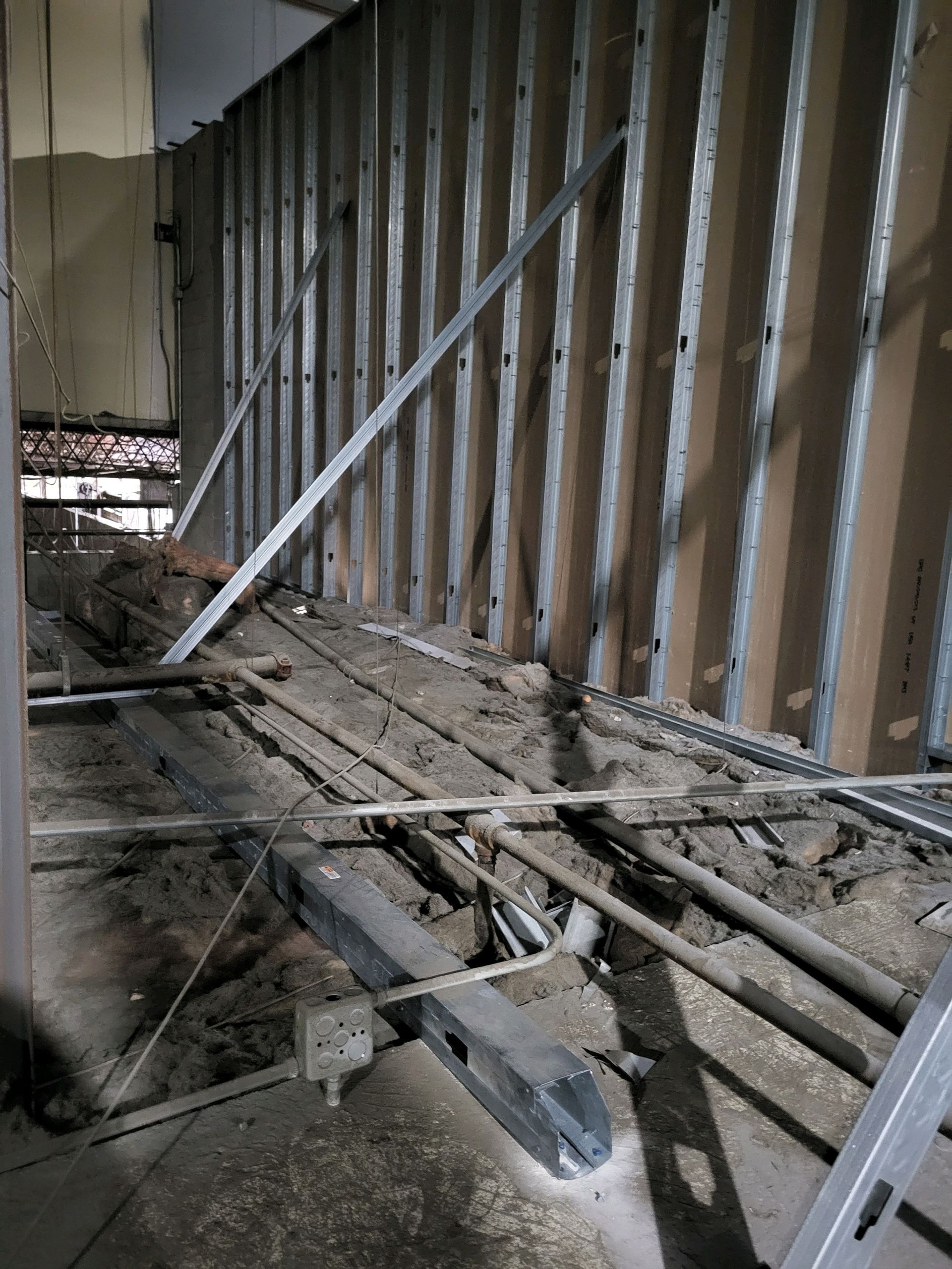 Interior construction site with exposed wooden wall framing, scattered lumber, and debris on the floor.
