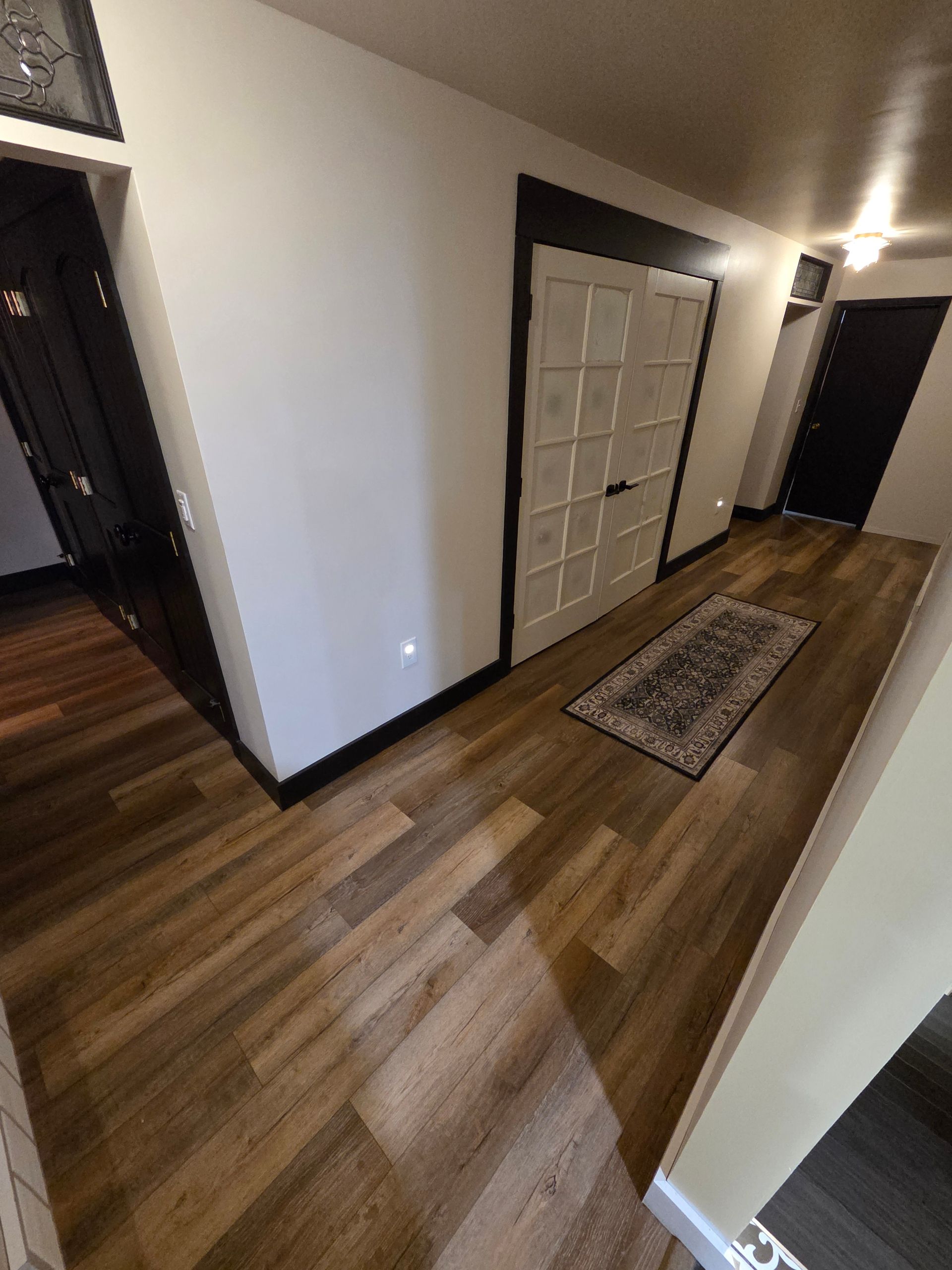 Hallway with wood floors, white walls, a closed closet door, and a narrow rug.