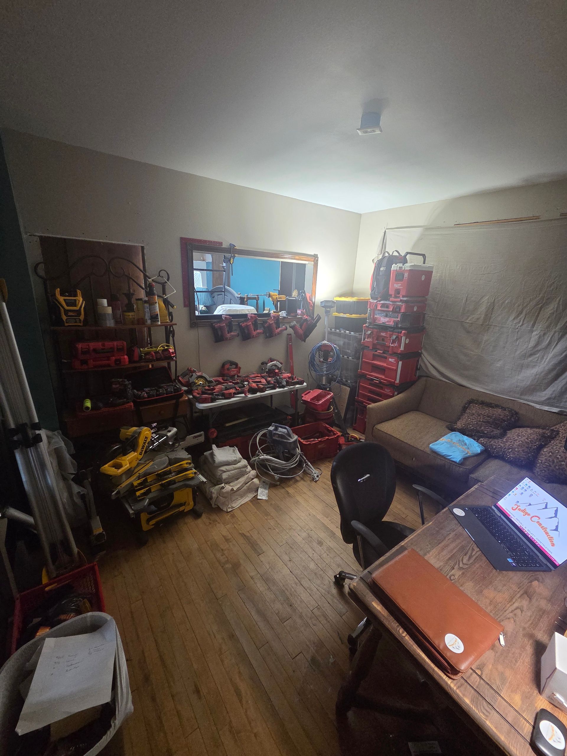 Cluttered living room with toys, shelves, a couch, and a desk with a laptop and tablet.