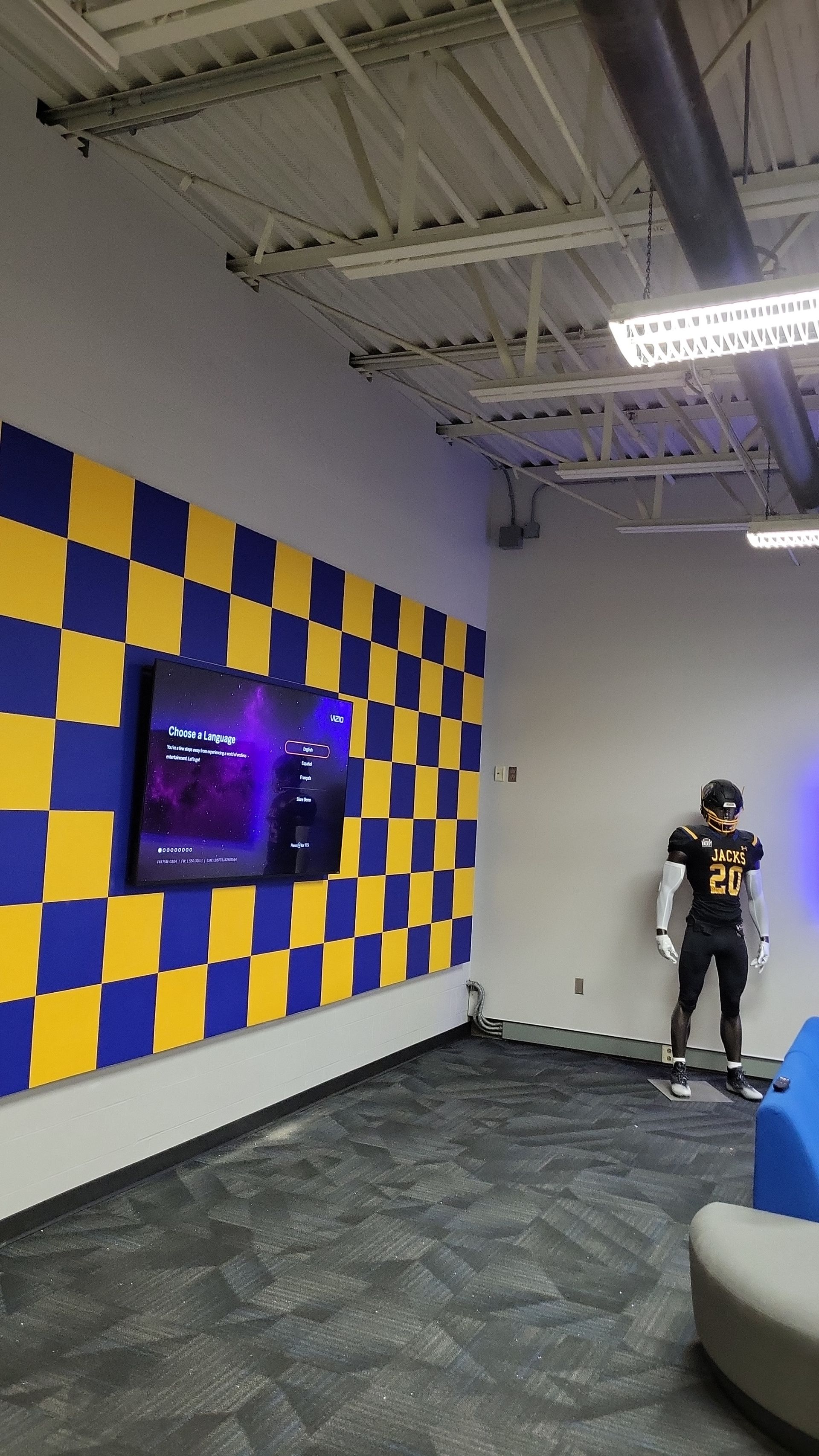 Yellow-and-blue checkered wall with a TV screen in a modern lounge, and a person standing near the back wall.