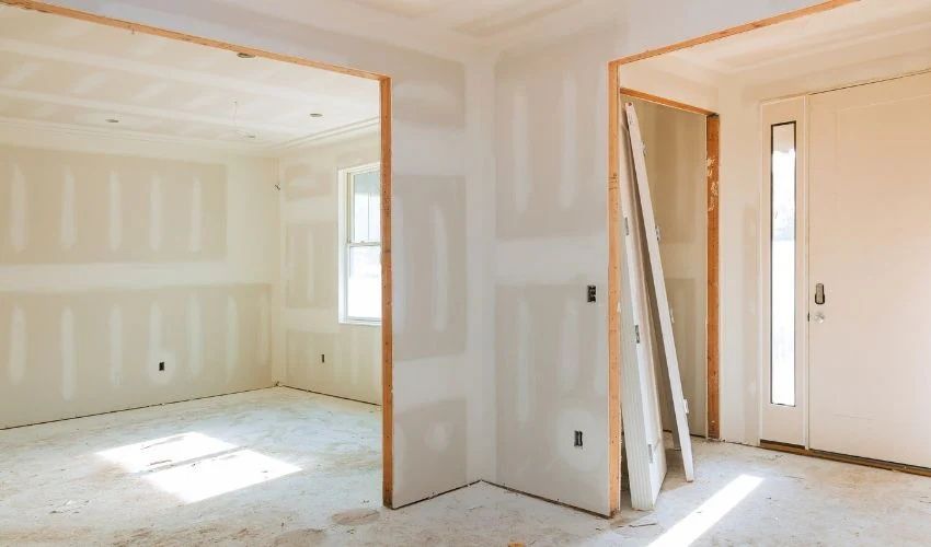 Empty unfinished room with drywall, a doorway, and sunlight streaming in through windows.