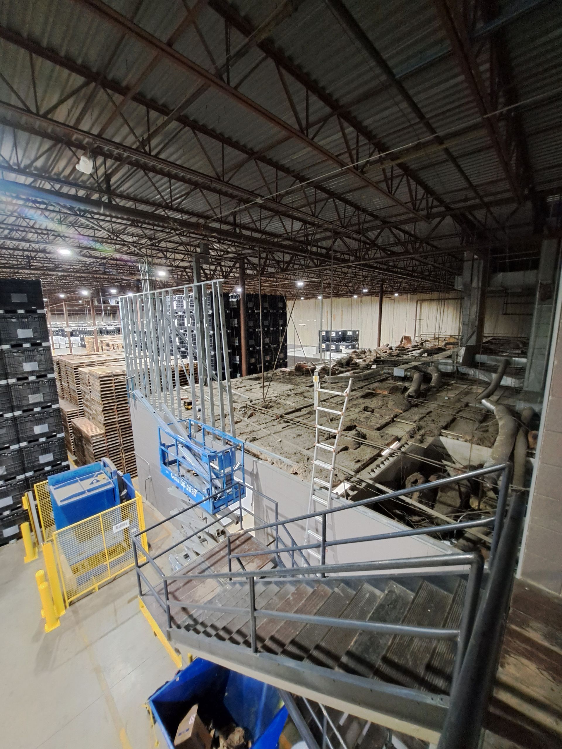 Inside a warehouse, workers install a metal mezzanine and staircase under construction.