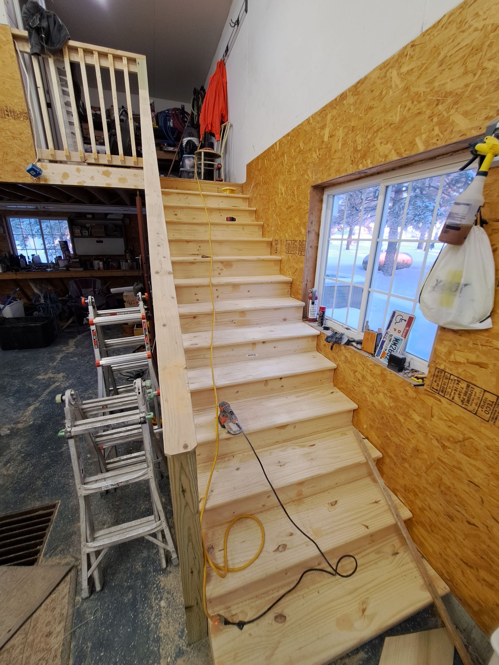 Interior under construction with wooden stairs, loft railing, and cord on unfinished walls