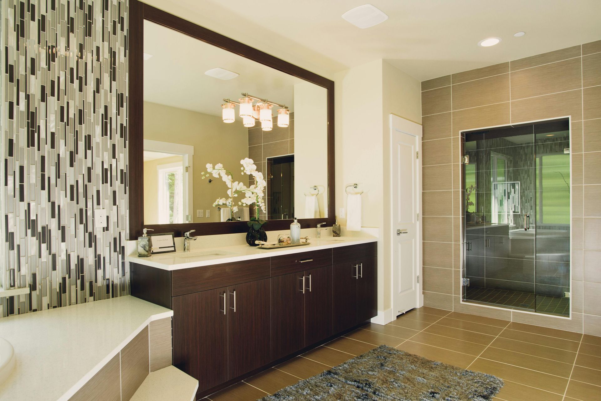 Modern bathroom vanity with dark wood cabinets, large mirror, mosaic accent wall, and glass shower enclosure