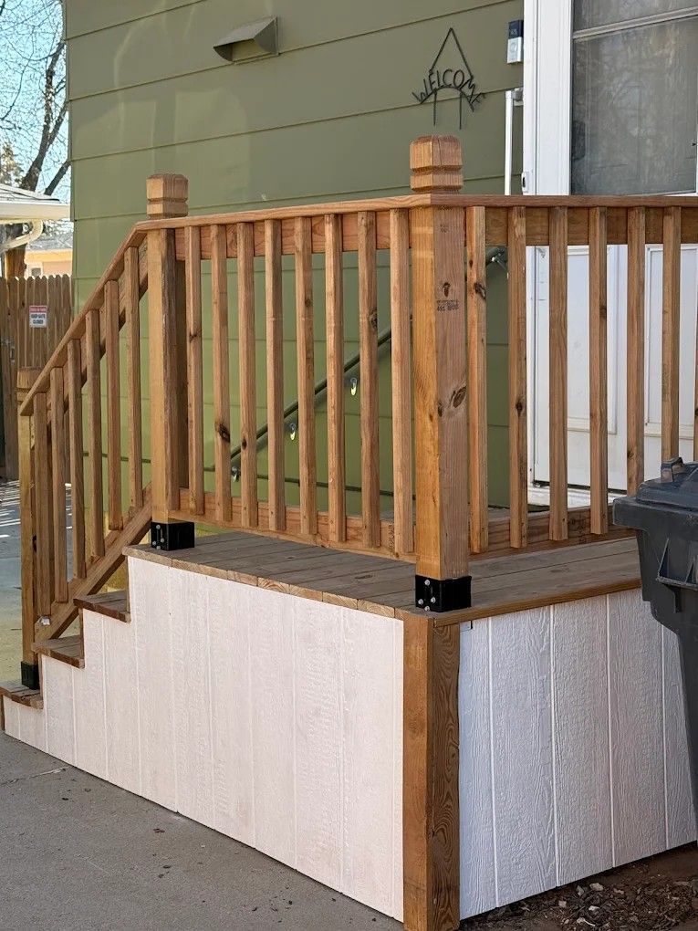 Wooden deck with railing and stairs beside a house over a white skirting foundation
