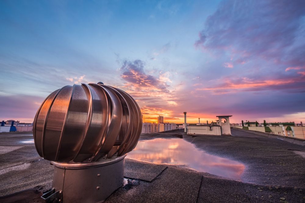 Rooftop wind turbine against a colorful sunset sky. Wet roof reflects the sky’s colors. — R&M Sheetmetal Nowra Metal Roofing in South Nowra, NSW