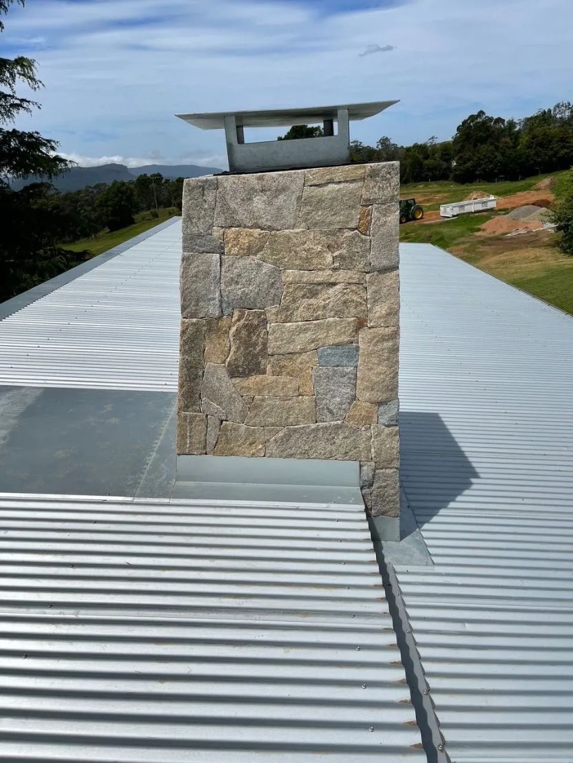 Stone chimney on a corrugated metal roof, with a mountain view in the background. — R&M Sheetmetal Nowra Metal Roofing in South Nowra, NSW