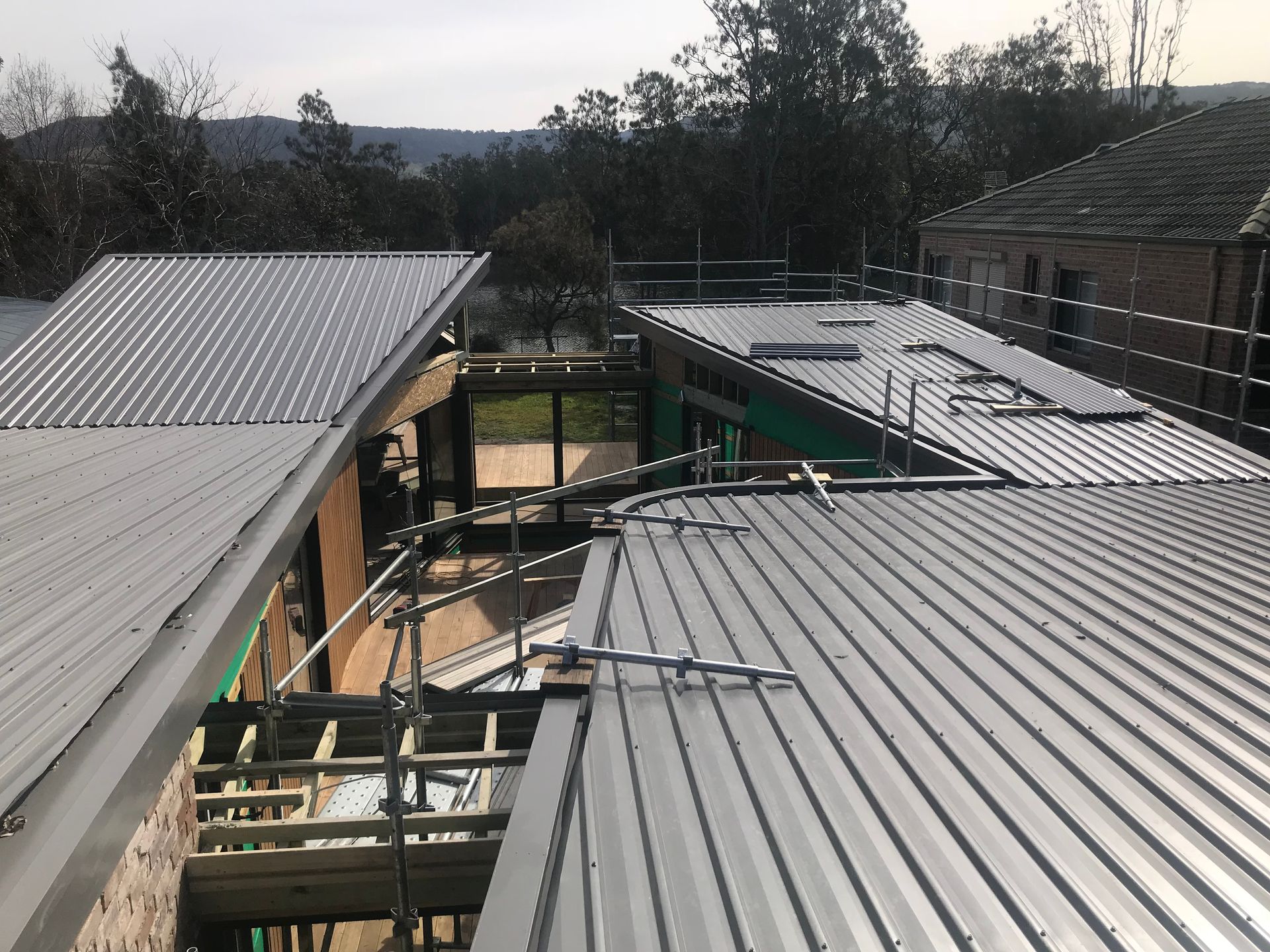 Metal roof installation on a multi-level building, scaffolding present, trees and sky in the background. — R&M Sheetmetal Nowra Metal Roofing in South Nowra, NSW