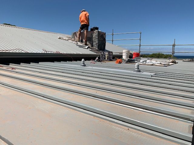 Person on a roof repairing a chimney. The roof is metal and the sky is blue. — R&M Sheetmetal Nowra Metal Roofing in South Nowra, NSW