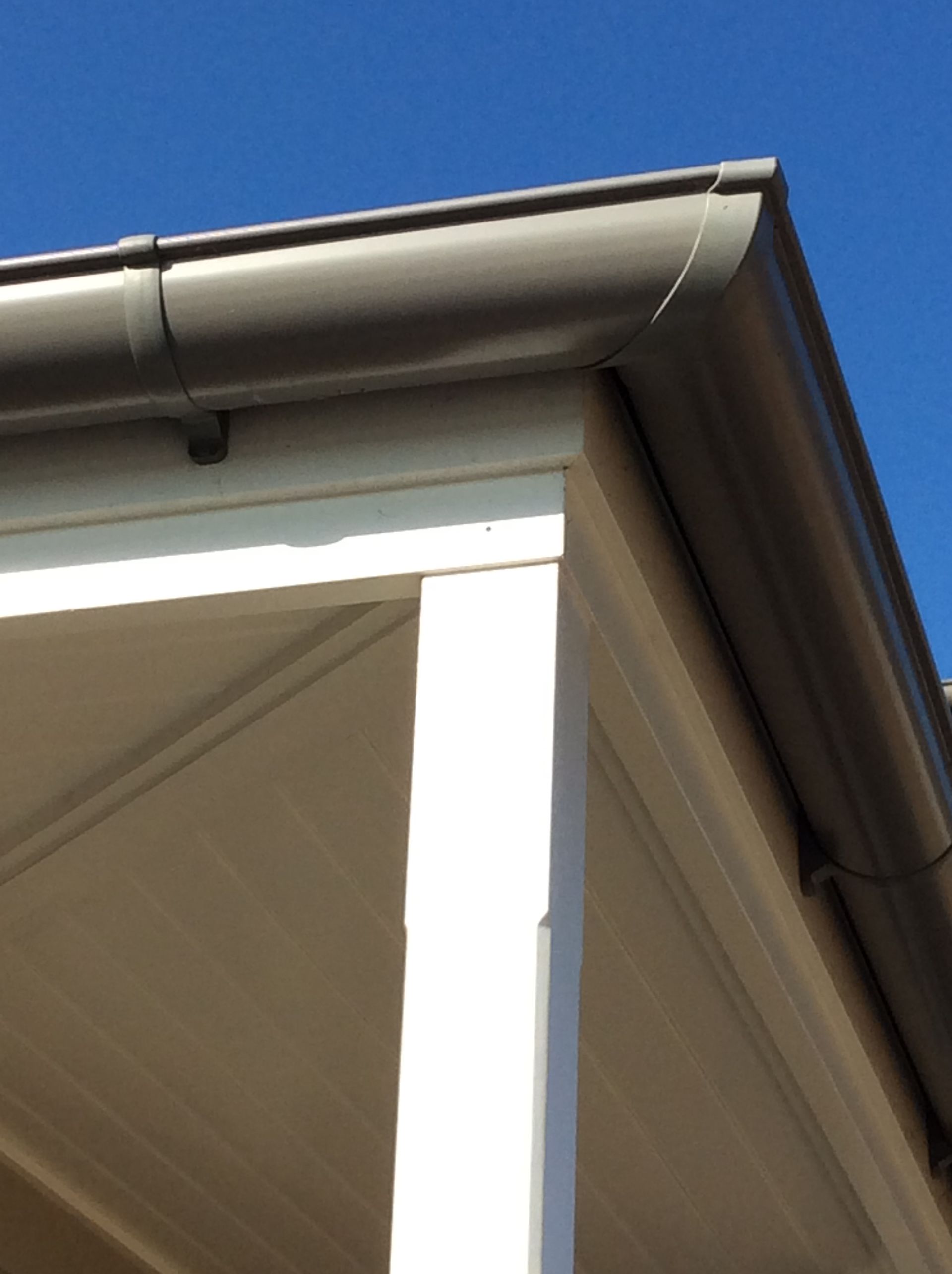 Brown guttering on a white building corner against a clear blue sky. — R&M Sheetmetal Nowra Metal Roofing in South Nowra, NSW