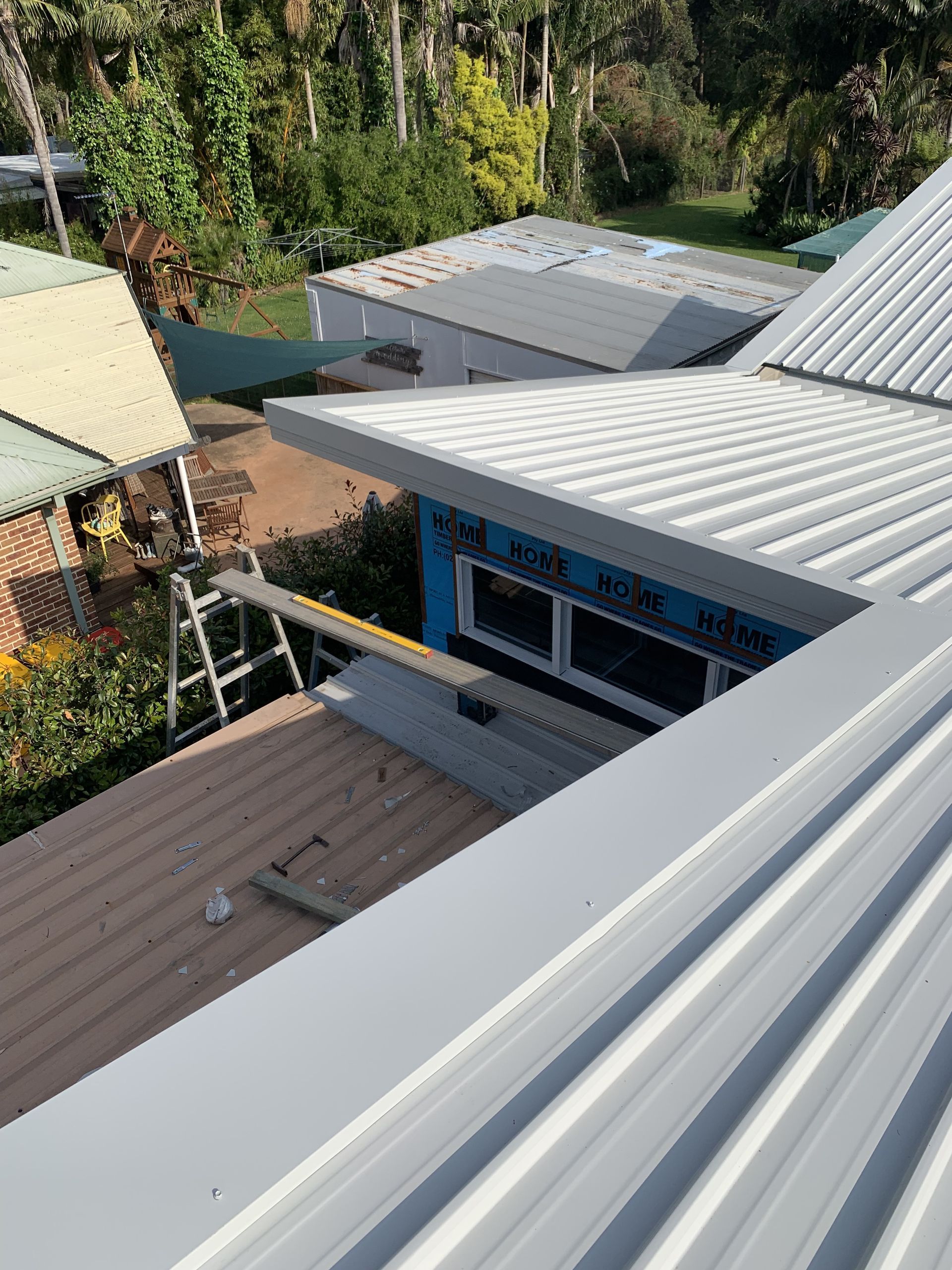 Overhead view of corrugated metal roofs of buildings, with a ladder and foliage visible. — R&M Sheetmetal Nowra Metal Roofing in South Nowra, NSW