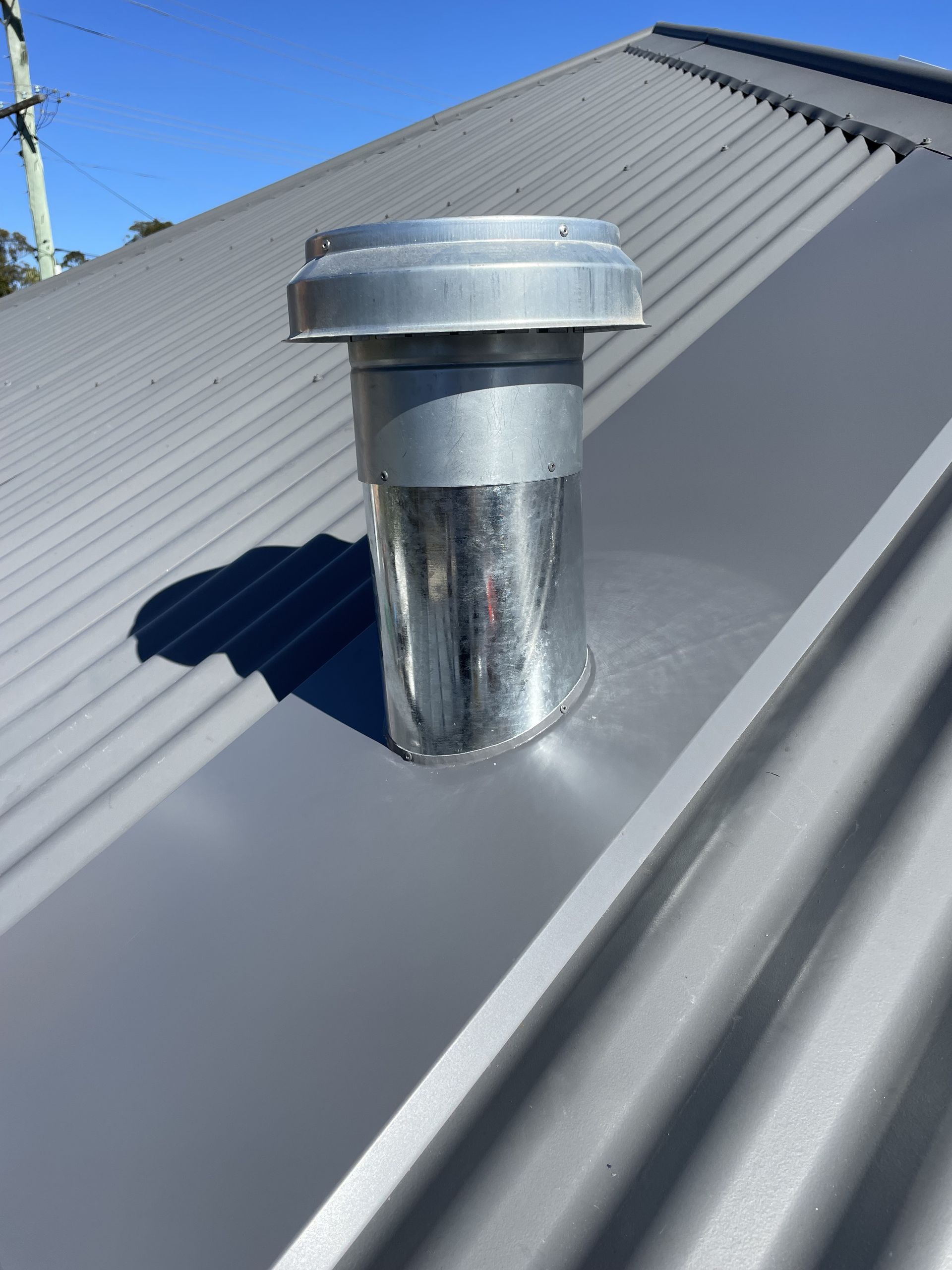 Metal exhaust vent on a gray metal roof under a blue sky. — R&M Sheetmetal Nowra Metal Roofing in South Nowra, NSW