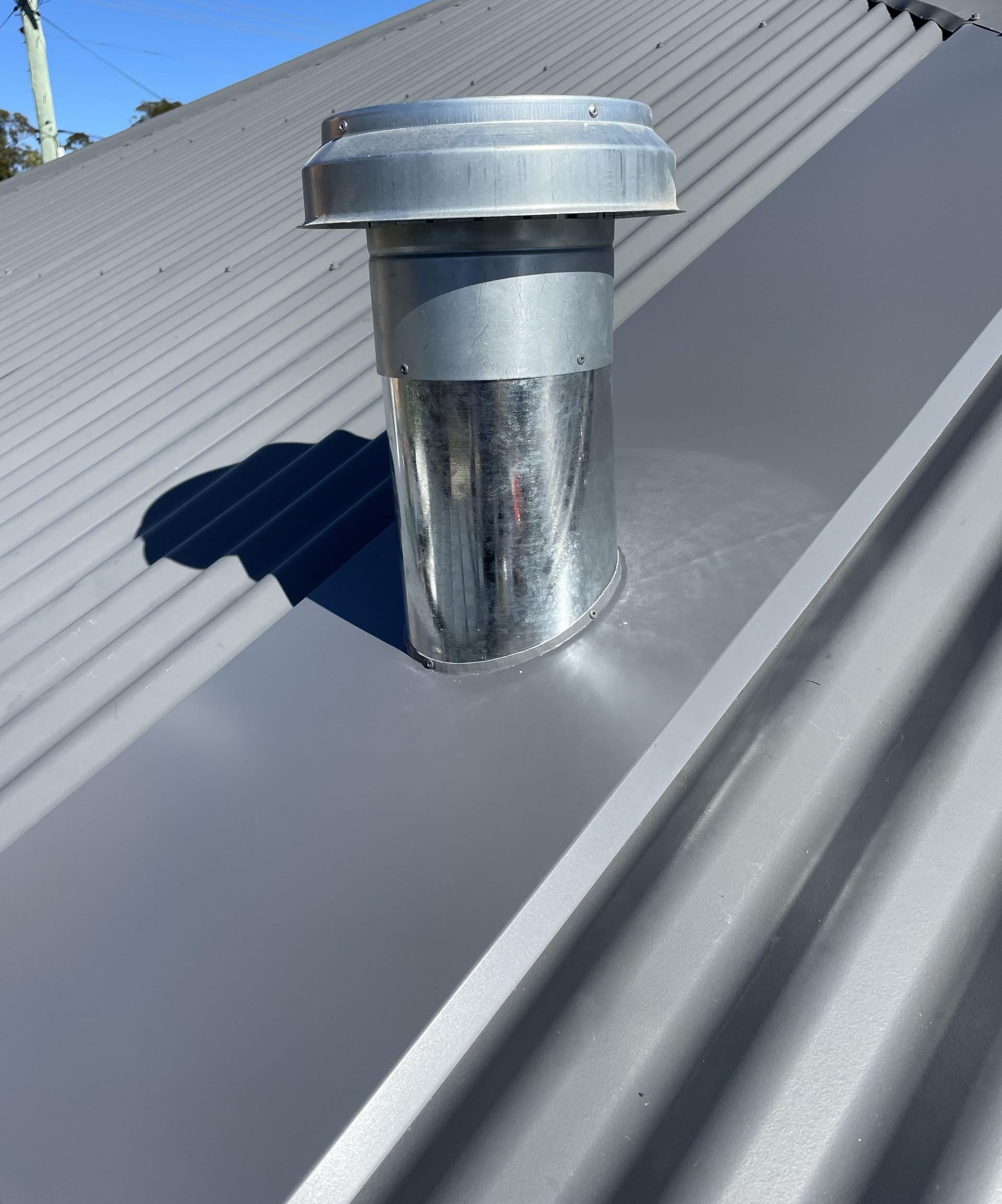 Metal exhaust vent on a gray corrugated metal roof under a blue sky. — R&M Sheetmetal Nowra Metal Roofing in South Nowra, NSW