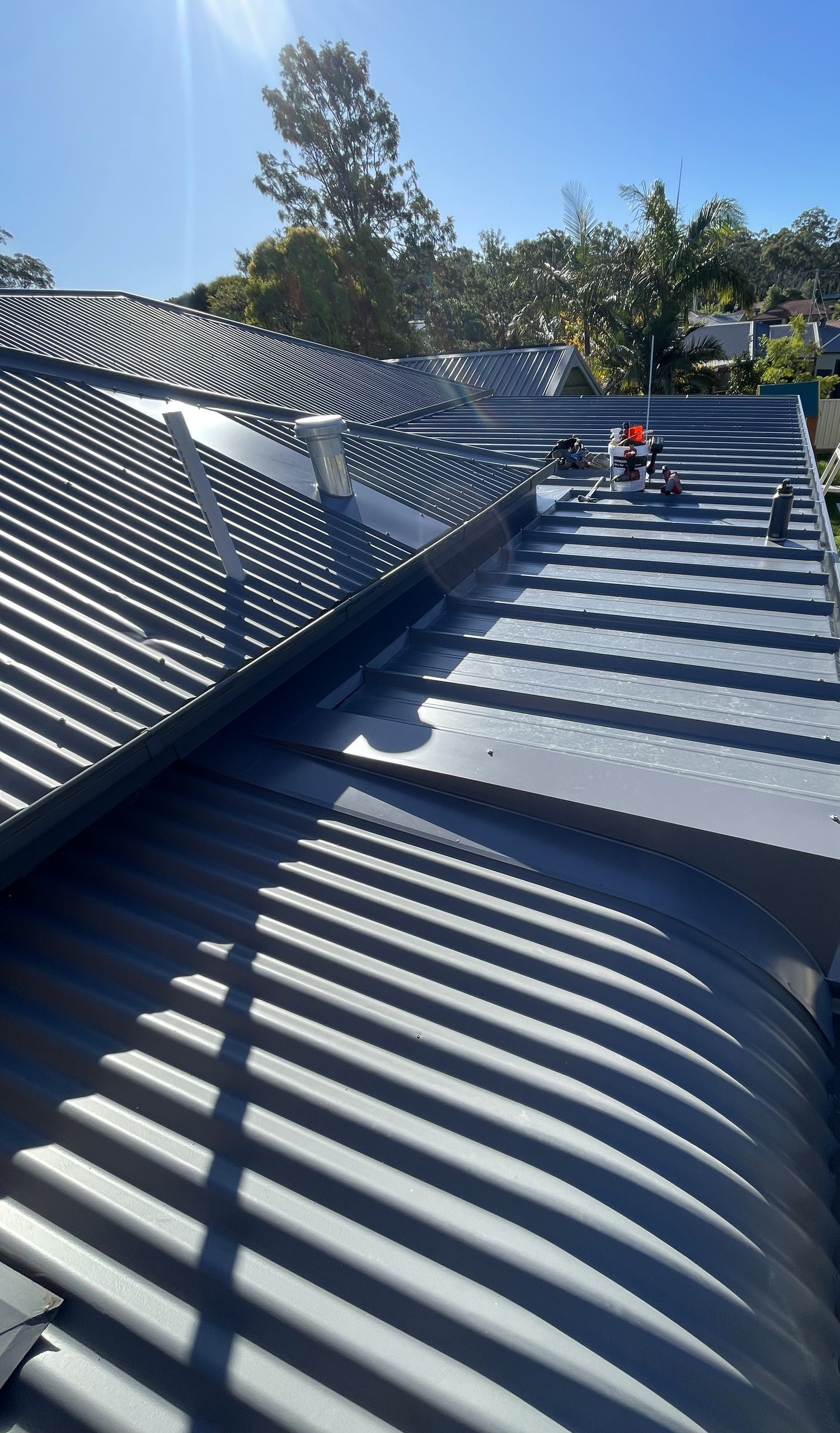 A grey corrugated metal roof with solar panels installed, workers on the roof under a bright blue sky. — R&M Sheetmetal Nowra Metal Roofing in South Nowra, NSW