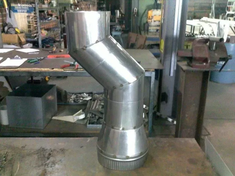 Stainless steel chimney pipe with angled section, on a metal workbench in a workshop. — R&M Sheetmetal Nowra Metal Roofing in South Nowra, NSW