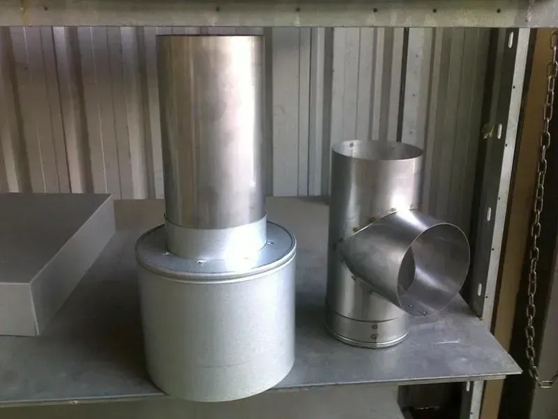 Two metal chimney components on a shelf, one straight, one with a side pipe. — R&M Sheetmetal Nowra Metal Roofing in South Nowra, NSW