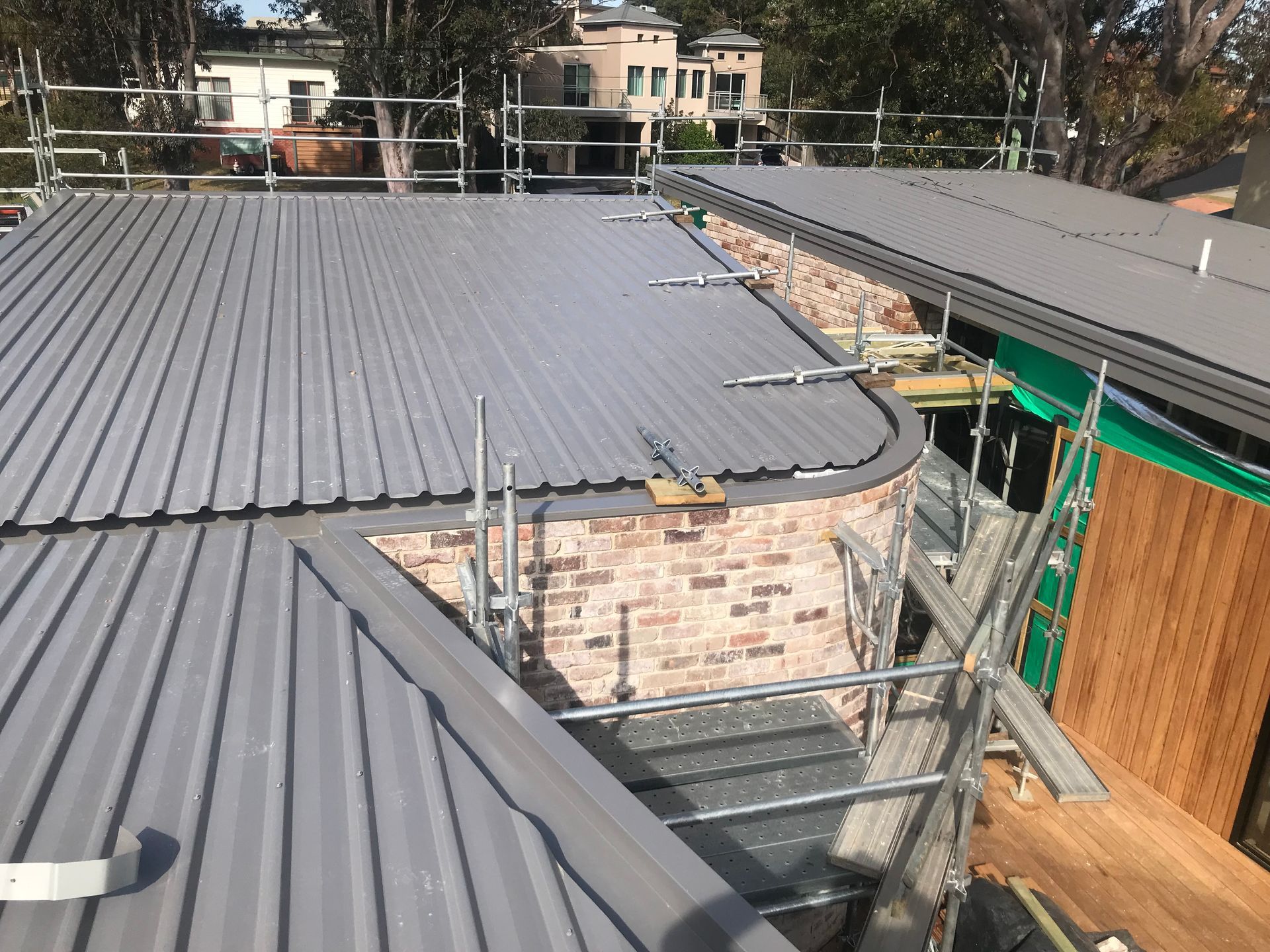 A roof with corrugated metal panels and brick wall under construction with scaffolding. — R&M Sheetmetal Nowra Metal Roofing in South Nowra, NSW