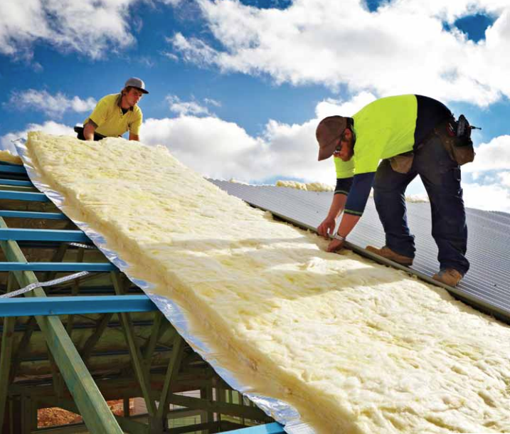 Two workers installing insulation on a roof under a blue sky with clouds. One cuts insulation; the other assists. — R&M Sheetmetal Nowra Metal Roofing in South Nowra, NSW