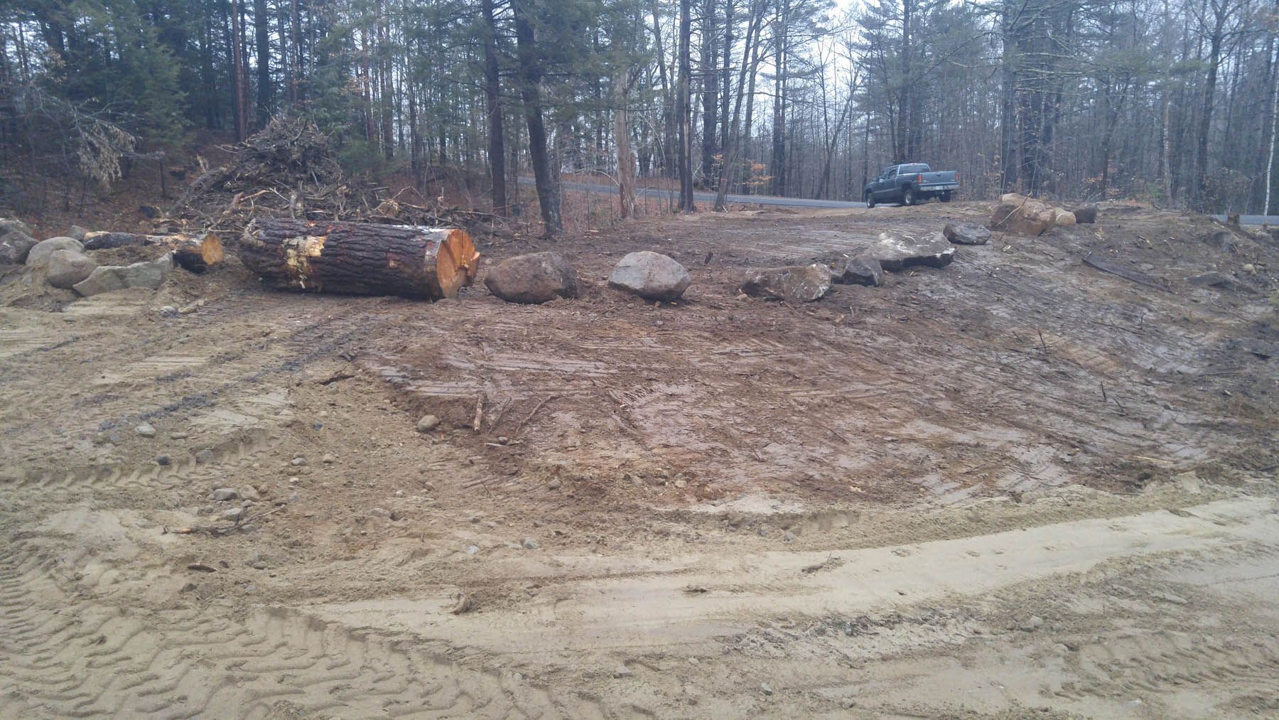 Dirt path with logs, rocks, and vehicle in a forest clearing.