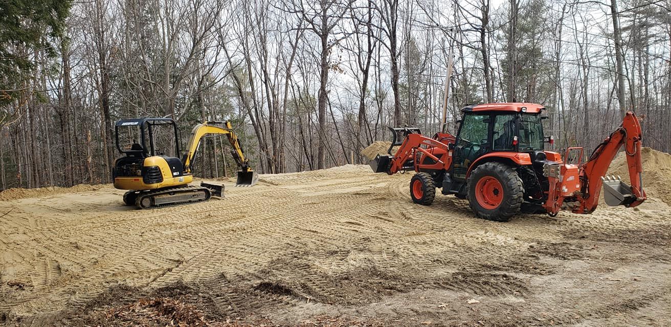 Two excavators working on a construction site. One is yellow, the other is orange. Trees are in the background.