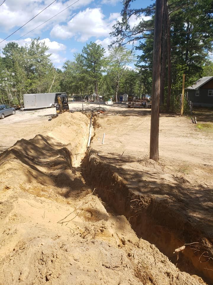 A long trench dug in sandy soil with a utility pole and wires nearby; a rural setting.